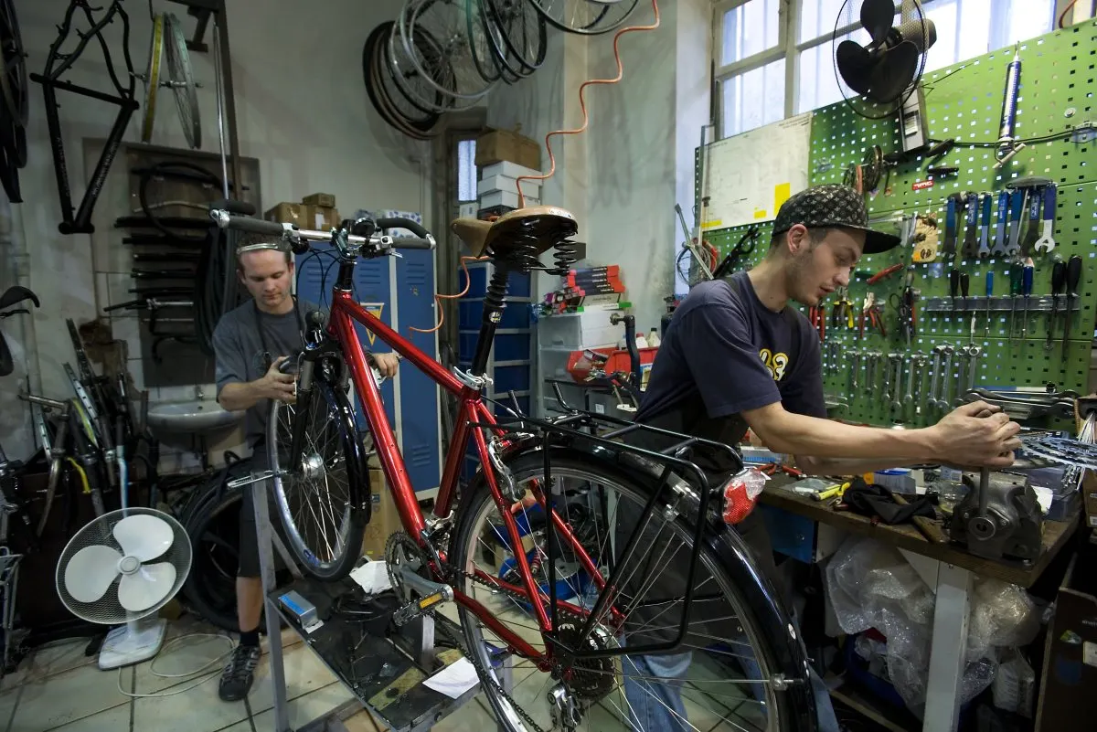 Twee mannen repareren fietsen in een werkplaats met gereedschap.